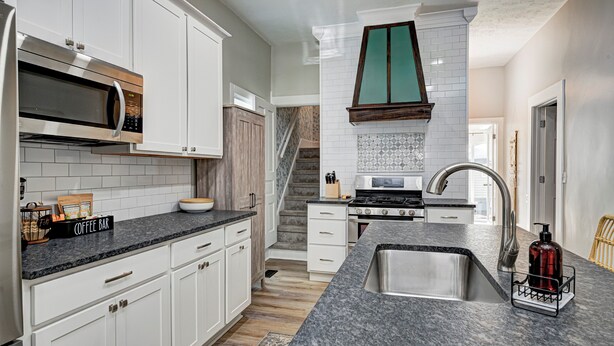 A modern kitchen with white cabinets, a granite countertop, a stainless steel sink, and a coffee bar.