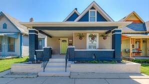 A two-story house with a front porch, a green door, and potted plants.