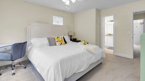 A bedroom with a bed, a desk, a chair, a ceiling fan, and a door leading to another room. - Minutes from Cherry Point (Havelock)