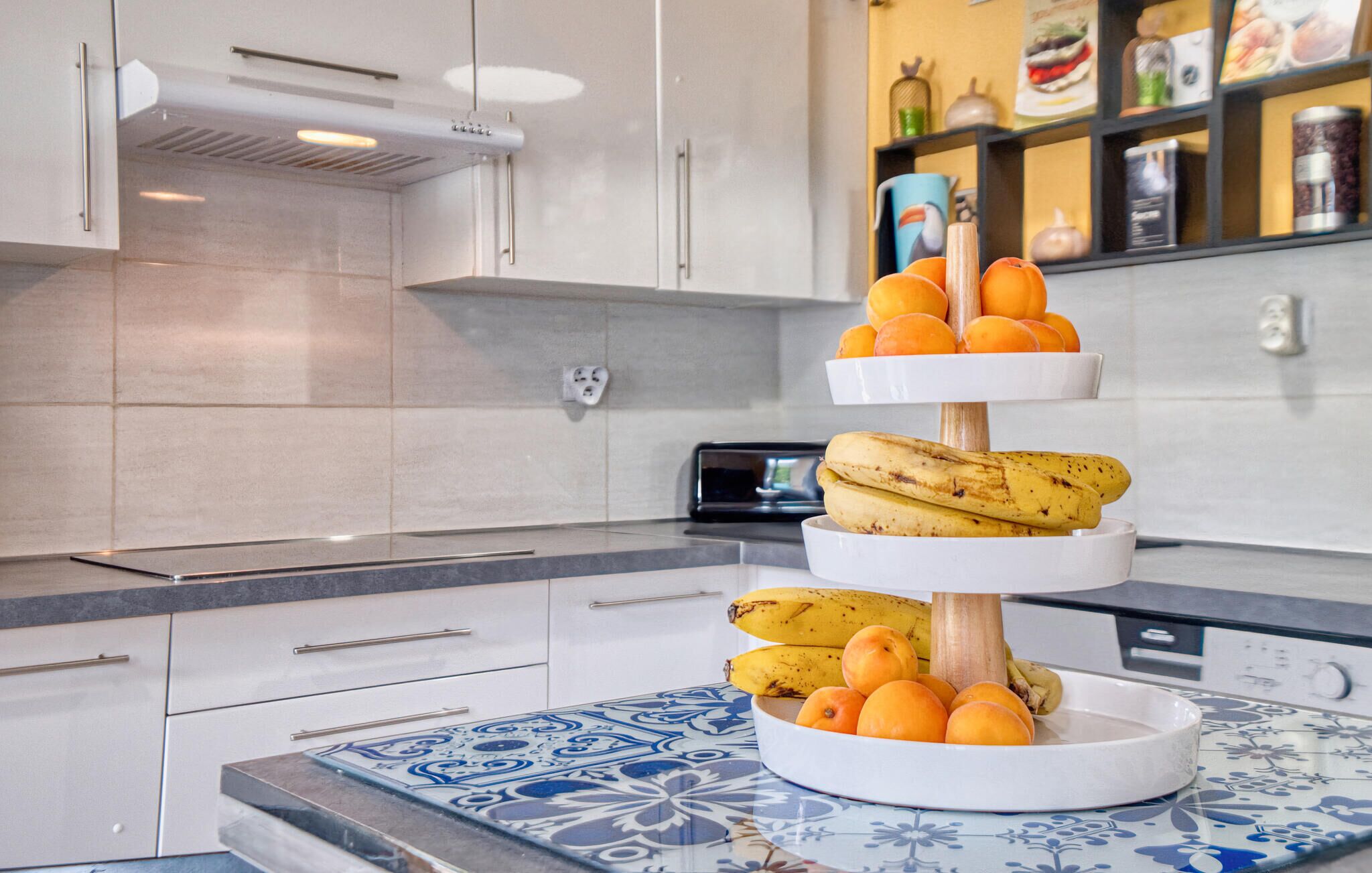 A kitchen with a three-tiered fruit stand holding bananas and oranges.