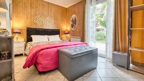 A bedroom with a bed, bedside tables, a nightstand, a window with curtains, and a view of the outdoors.