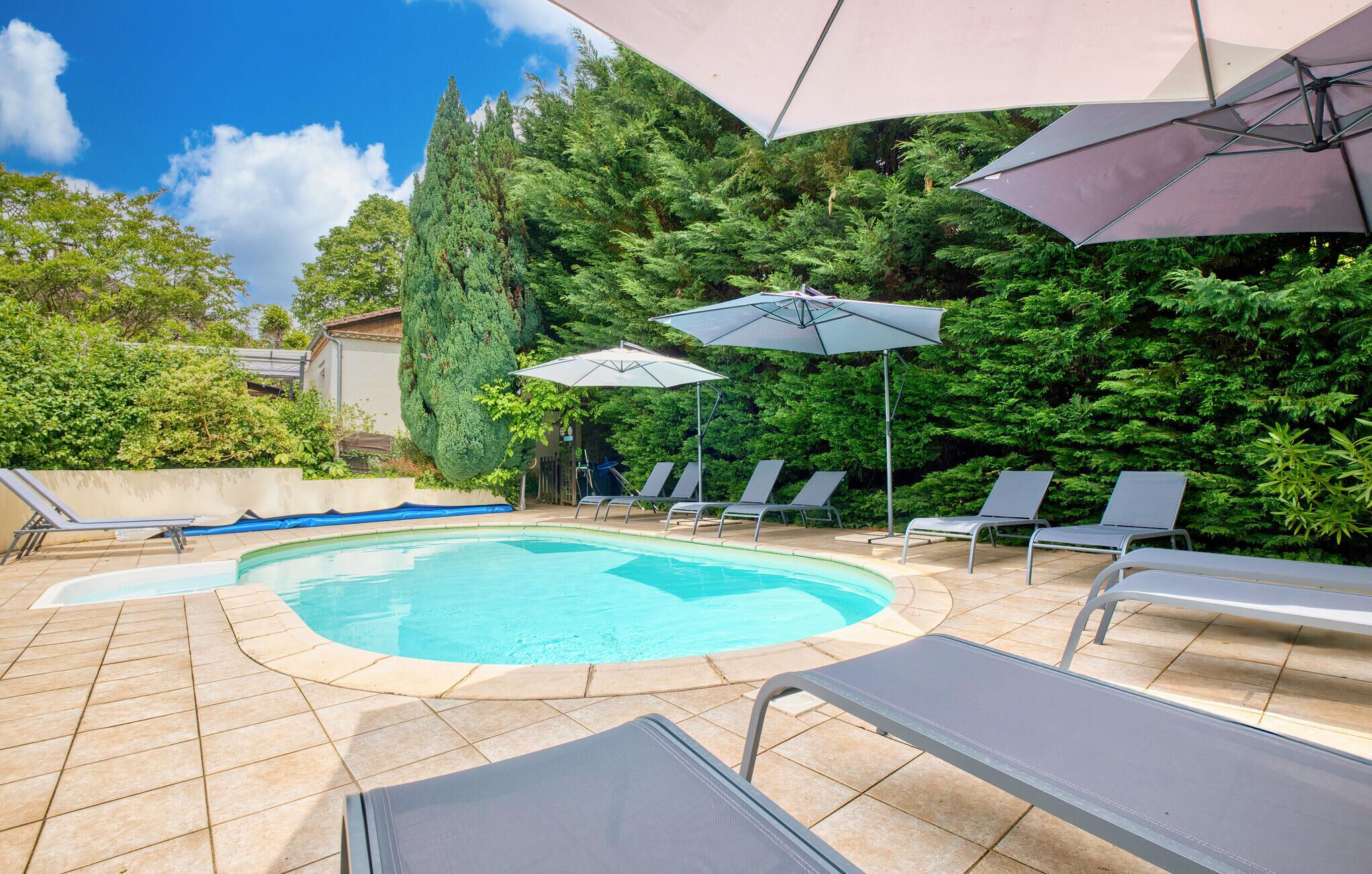Une piscine dont le fond est recouvert de carrelage, entourée de chaises longues et de parasols.