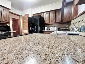 Eine Küche mit Granit Arbeitsplatten, einem schwarzen Kühlschrank, einer Mikrowelle, einem Toaster und Holzschränken.