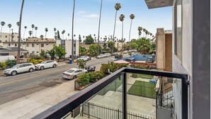 A balcony with a view of a street lined with palm trees and parked cars.