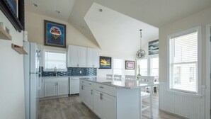 Una cocina moderna con armarios blancos, una isla grande y un comedor con mobiliario blanco.