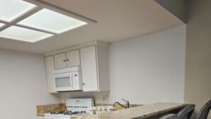A compact kitchen with white cabinets, a microwave, a stove, and a small island with chairs. - Charming 2-bedroom house in vibrant Las Vegas with WiFi, AC (Las Vegas)