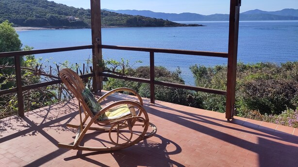 Une terrasse en bois avec un fauteuil en osier donnant sur une étendue d’eau et des montagnes lointaines.