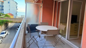 A balcony with a table and chairs, a sliding glass door, and a view of a street and buildings. - Les 3 Îles Location. Air-conditioned apartment 50m from Juan Les Pins beaches (Antibes)