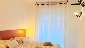 A neatly made bed with a patterned bedspread, a bedside lamp, and a rolled towel on the bed. - Les 3 Îles Location. Air-conditioned apartment 50m from Juan Les Pins beaches (Antibes)