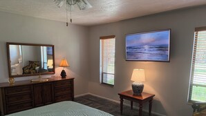 A bedroom with a large bed, a dresser with a mirror, a lamp, and a painting on the wall.
