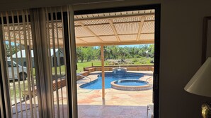 A view through a window to a backyard with a swimming pool, patio, and a car parked outside.