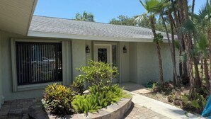 A house with a tiled roof, a brick pathway, and a landscaped garden with palm trees and shrubs.