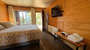 Une chambre avec un lit, un banc avec des serviettes, un téléviseur fixé au mur et une vue sur l’extérieur.