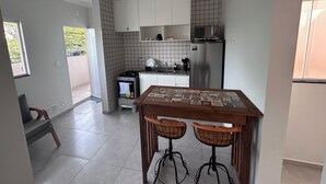 A modern kitchen with white cabinets, a gas stove, a microwave, and a refrigerator. There is a dining table with two chairs in the foreground. - Comfort and practicality in the heart of Sorocaba (Jardim Santa Rosália Sorocaba)