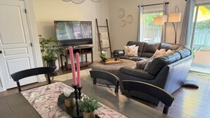 Una sala de estar con sofá, televisión y una mesa de comedor con mantel corrido floral.