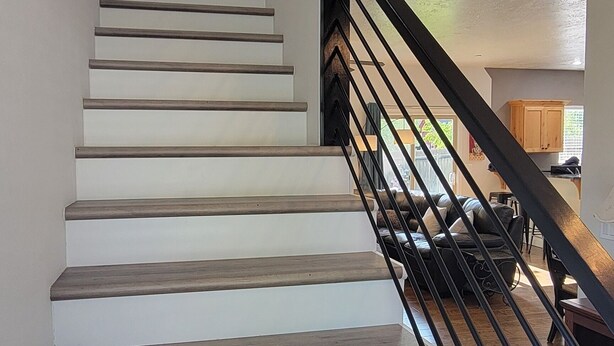 Una escalera con escalones de madera y barandilla negra, que conduce a una habitación con una puerta blanca y una planta.