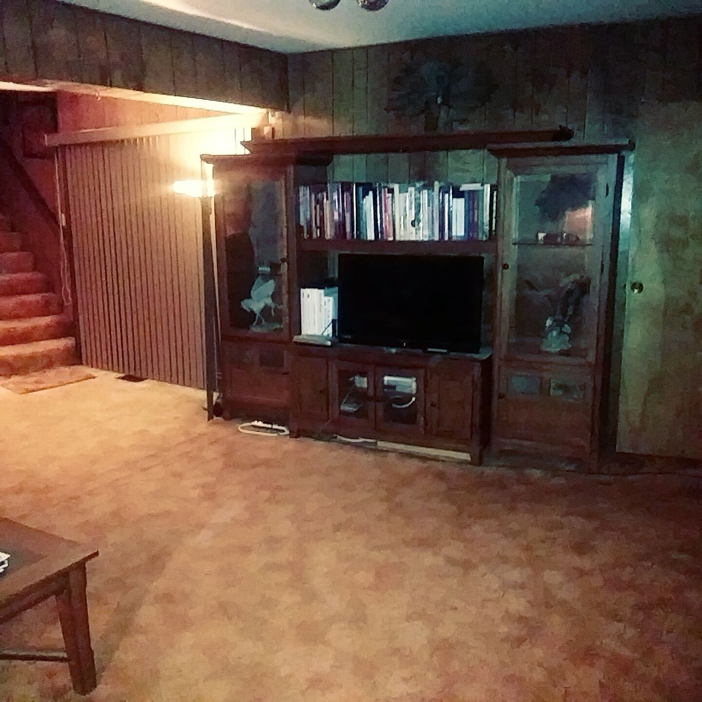 A living room with a wooden entertainment center, a flat-screen TV, and a staircase.