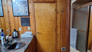 A compact kitchen with wooden paneling, a sink, a stove, and a window with a towel hanging.