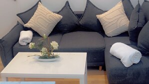 Uma sala de estar moderna com um sofá cinzento, almofadas brancas, uma mesa de centro branca e um pequeno vaso com flores.
