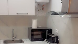 Uma cozinha compacta com pia, micro-ondas, torradeira e máquina de lavar.