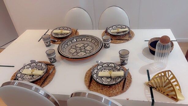 Mesa posta com pratos, tigelas e xícaras estampados, cercada por cadeiras.