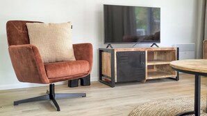 A modern living room with a brown leather chair, a wooden TV stand, and a round table. - 2 bedroom lovely home in Hellendoorn (Hellendoorn)