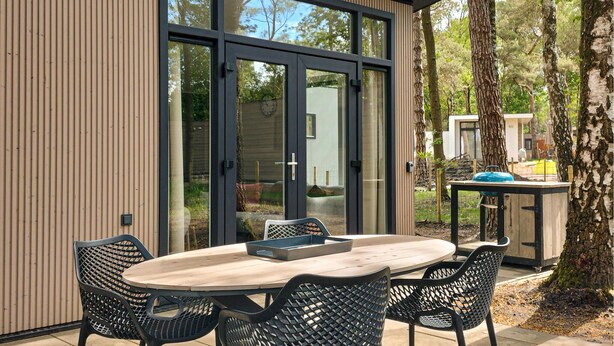 A modern outdoor dining area with a round table and four chairs, a grill, and a wooden wall. - Awesome home in Hellendoorn with WiFi (Hellendoorn)