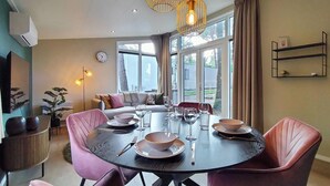 A dining area with a round table set for four, surrounded by pink chairs. There is a sofa and a dining table in the background with a view of the outdoors. - Awesome home in Hellendoorn with WiFi (Hellendoorn)