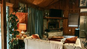 Ein gemütliches Wohnzimmer mit Kamin, einer Couch, einer Lampe und einem Fernseher.