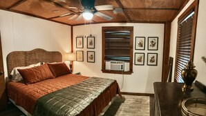 Ein Schlafzimmer mit einem Bett, einem Deckenventilator, einem Fenster mit Jalousien und gerahmten Bildern an der Wand.