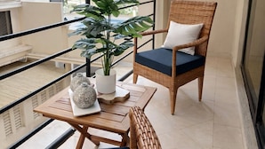 A balcony with wicker furniture, a potted plant, and a table with decorative items. - Elegant Modern Home (Dar es Salaam)
