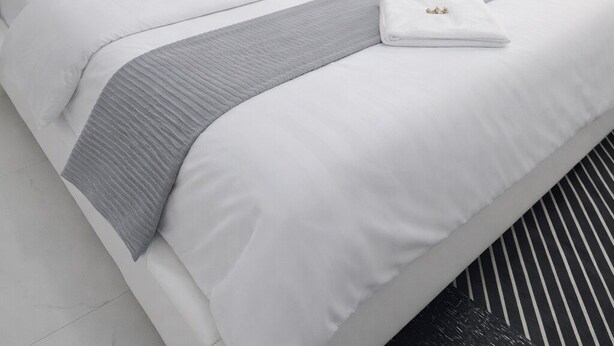 A modern hotel room with a neatly made bed, a bedside lamp, and a window with curtains. - Elegant Modern Home (Dar es Salaam)