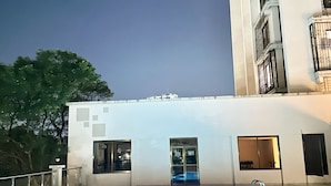 An outdoor swimming pool with a tiled deck, surrounded by a white building with multiple windows and balconies. - Elegant Modern Home (Dar es Salaam)