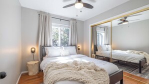 Ein Schlafzimmer mit Bett, Nachttisch, Spiegel und Deckenventilator.