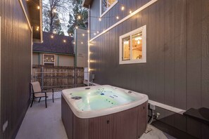 A hot tub in a backyard with a wooden fence, a chair, and string lights. - Peak Pursuit | Jacuzzi, Game Room, Sauna, Cent AC! (Big Bear)