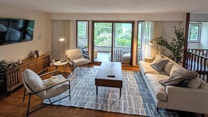 A modern living room with a sofa, armchairs, a coffee table, and a TV mounted on the wall.