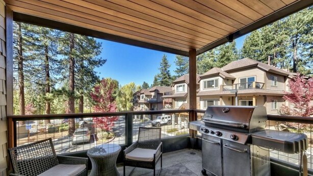 A covered outdoor patio with wicker furniture, a grill, and a view of residential buildings.