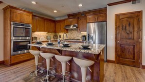 A kitchen with wooden cabinets, stainless steel appliances, a granite countertop, and bar stools.