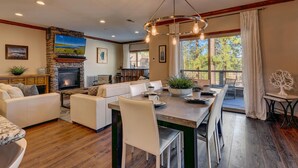 A spacious living room with a fireplace, a dining area with a large table, and a view of the outdoors.