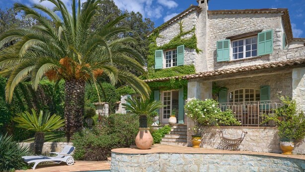 Una casa de piedra con piscina, rodeada de abundante vegetación y palmeras.