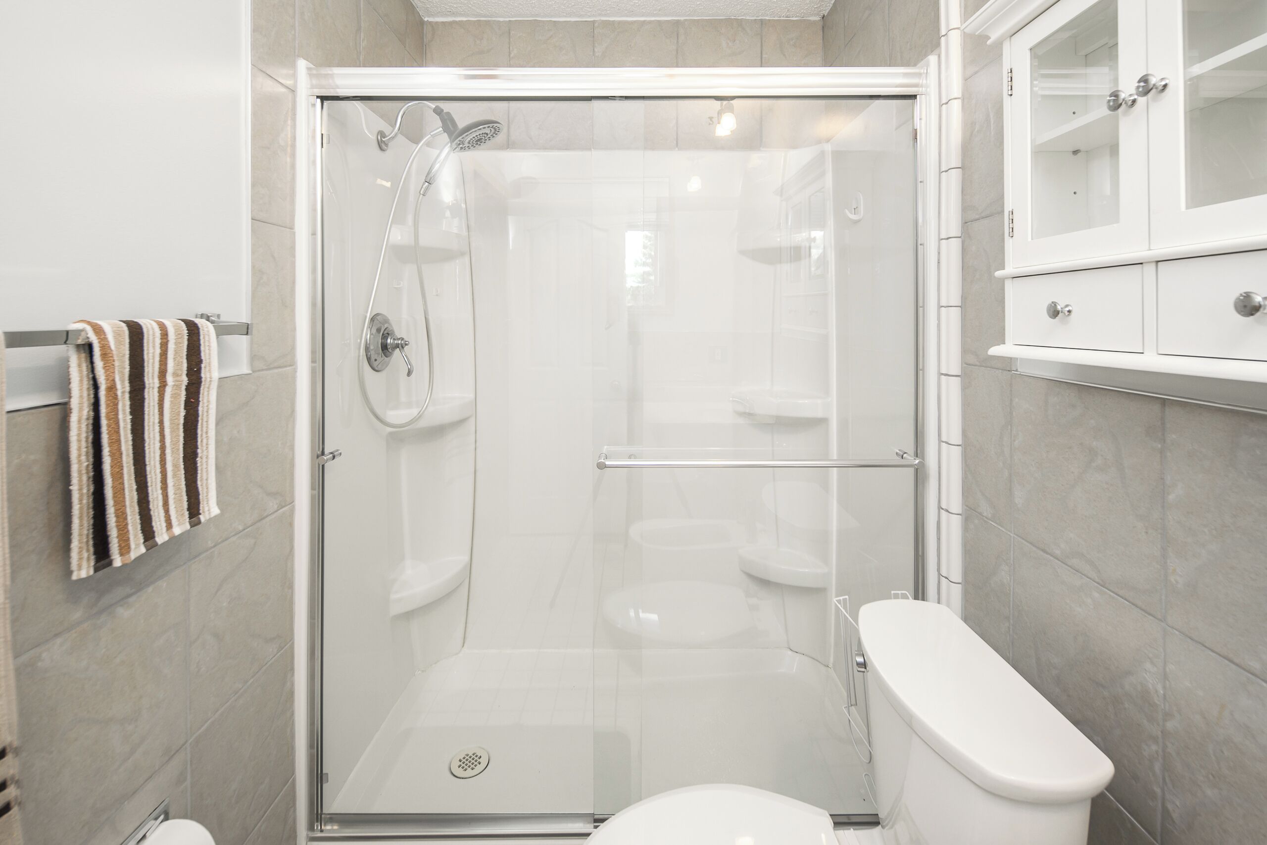 Ein modernes Badezimmer mit einer Duschkabine aus Glas, einer weißen Toilette und einem Schrank mit Glastür.
