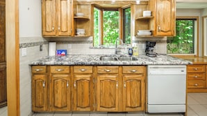 A kitchen with wooden cabinets, a granite countertop, a dishwasher, and a window with a view of greenery. - Spacious Home Near Stampede & Downtown Fully Fenced Yard Double Garage Pet OK (Calgary)