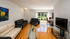 A living room with a sofa, two armchairs, a coffee table, a TV, and a painting on the wall. - Spacious Home Near Stampede & Downtown Fully Fenced Yard Double Garage Pet OK (Calgary)