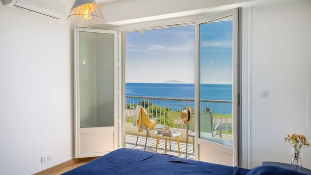 Un dormitorio con un gran ventanal corredera que da a un balcón con vistas al mar.