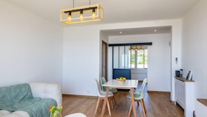 Una sala moderna con un sofá, una mesa de comedor y sillas. Hay una ventana con persianas, un radiador y una lámpara colgante.