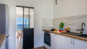 Una cocina moderna con vista al mar, un comedor con mesa y sillas, y un ventanal corredero que da a un balcón.