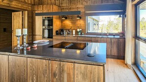 A modern kitchen with wooden cabinetry, a central island with a built-in stovetop, and a large window providing a view of the outdoors. - 4 bedroom stunning home in Eggedal (Eggedal)