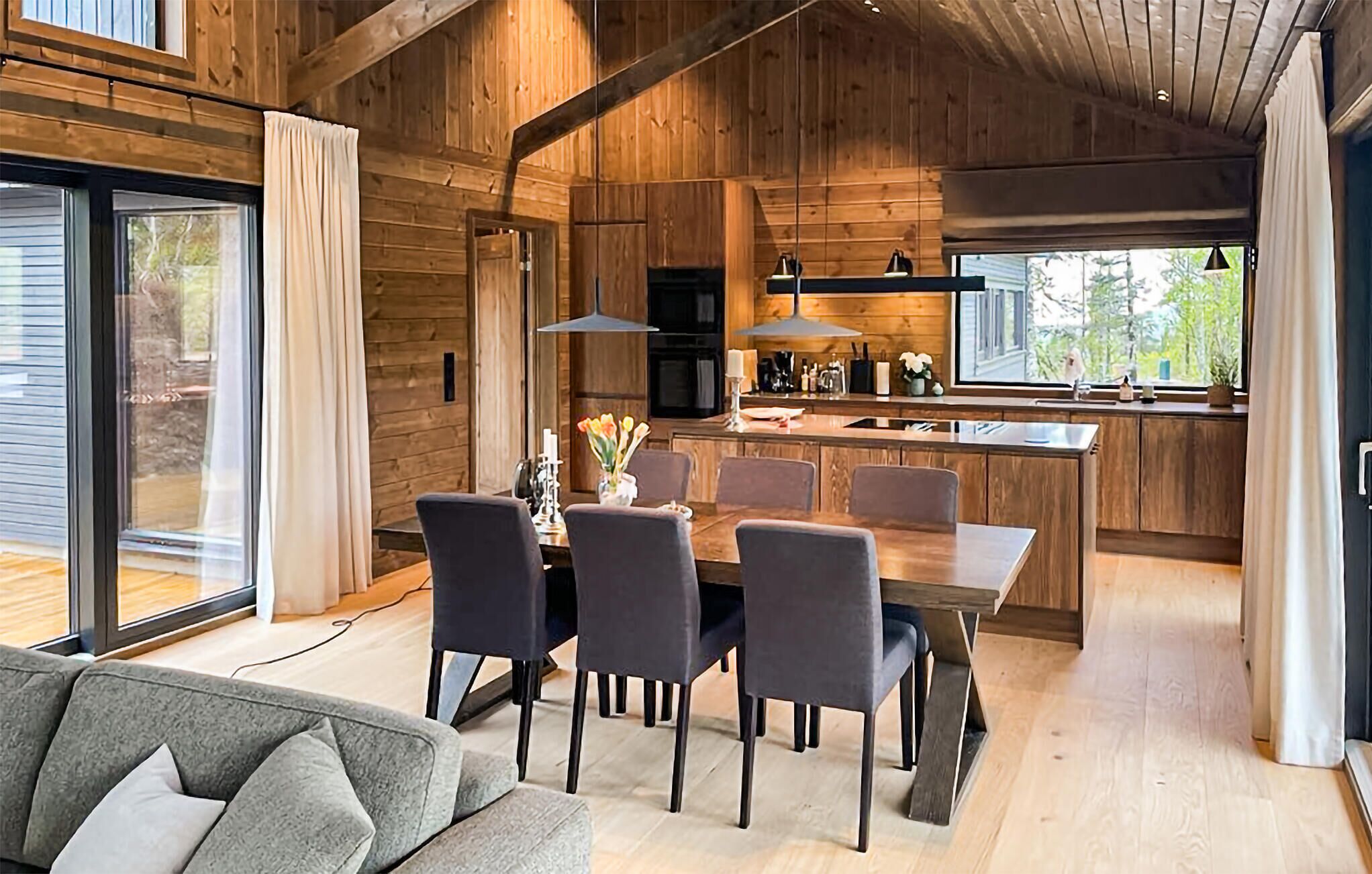 Una cucina moderna con pareti in legno, un'area pranzo con tavolo e sedie, e un'ampia finestra che offre luce naturale.