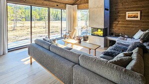 A modern living room with a large sofa, a fireplace, and large windows offering a view of the outdoors. - 4 bedroom stunning home in Eggedal (Eggedal)