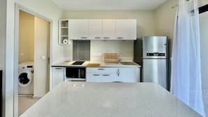 A compact kitchen with white cabinets, a stainless steel refrigerator, a microwave, and a built-in washing machine.